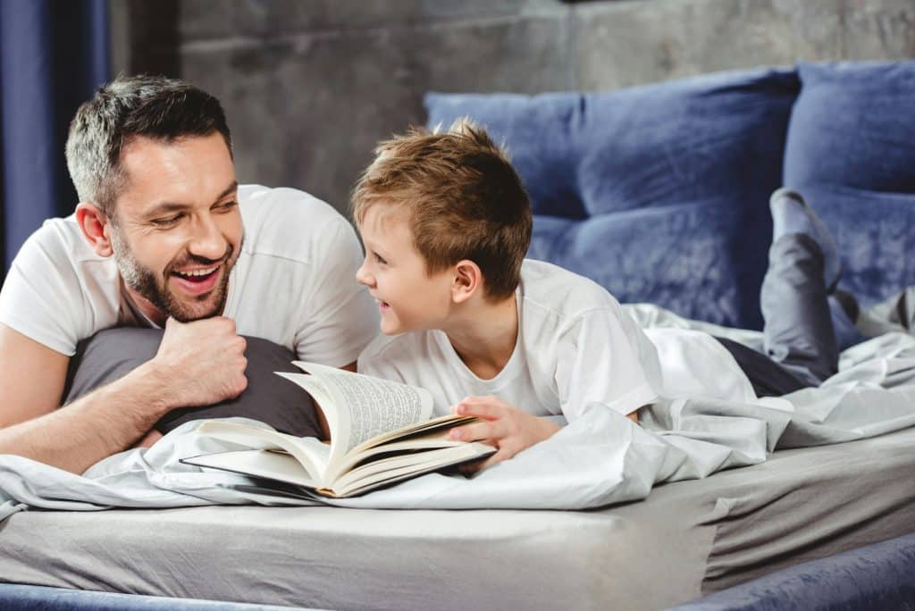 Smiling father and son reading book in bed