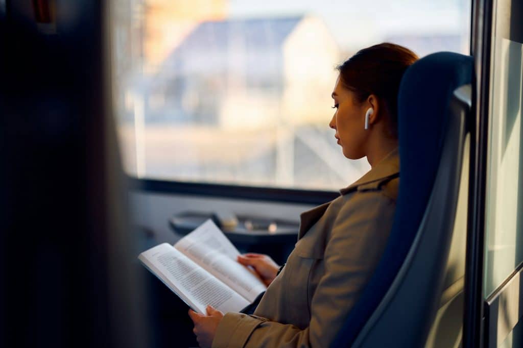 Young female passenger reading book while traveling by train.
